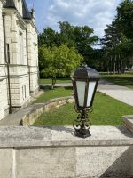 Dekoratívna lampa pri historickej budove s parkom a stromami.