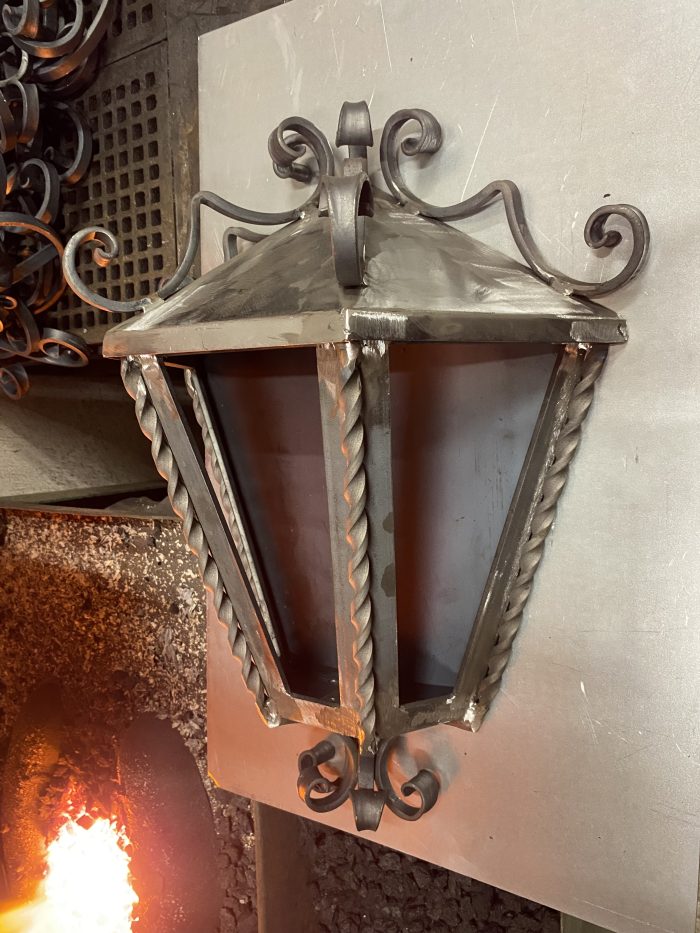 Kovaná lampa s ornamentmi nad ohňom, ručná práca.